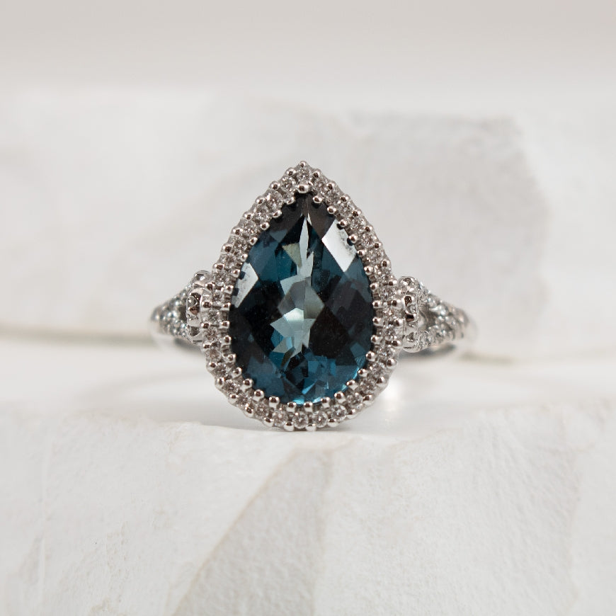 18KW London Blue Topaz & Diamond Halo Ring
18K White Gold Pear Shaped London Blue Topaz & Diamond Halo Ring
3.16 Carat Pear Shaped London Blue Topaz
0.22 Total Natural Diamond Weight of SI Clarity, GH Colour
Finger Size 6.25