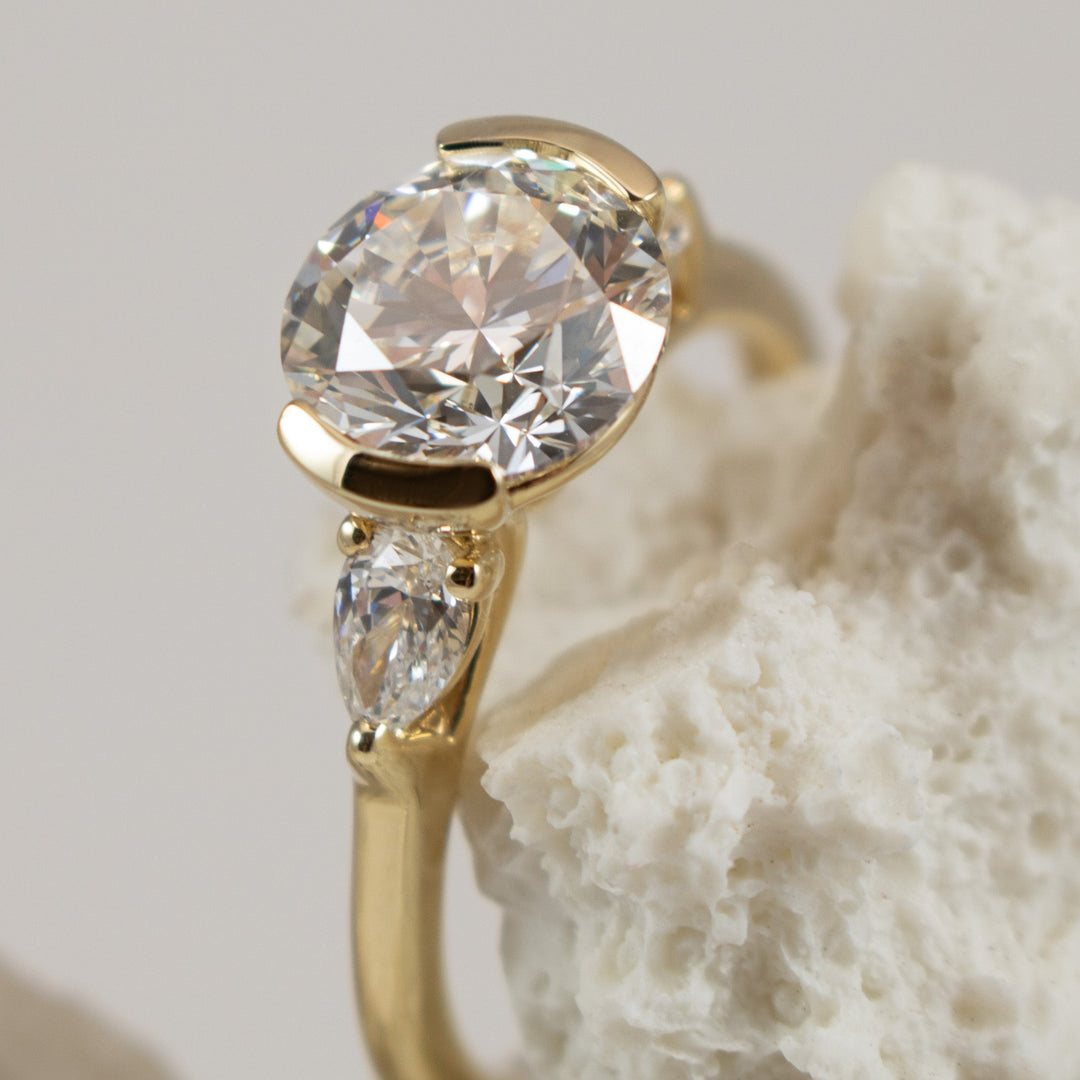 Gold ring with a large diamond and smaller gemstone on a textured beige background